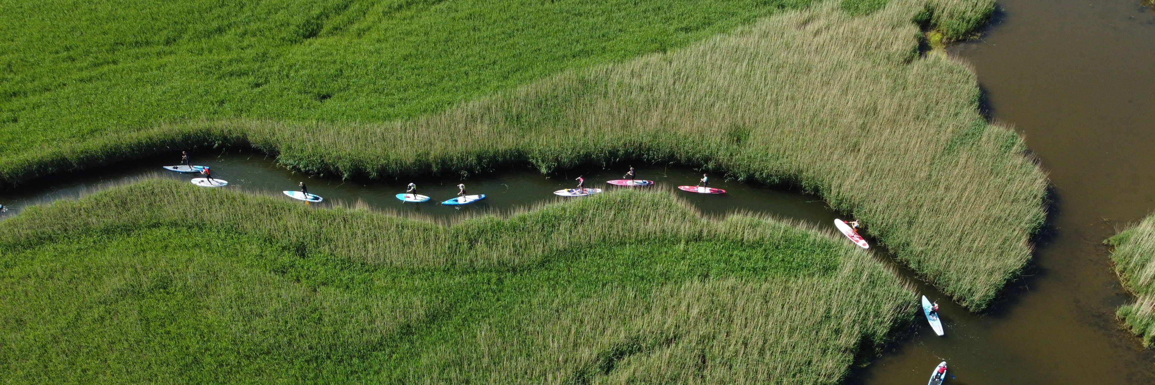 Mennesker på SUP-board padler gennem en smal kanal ved fjorden